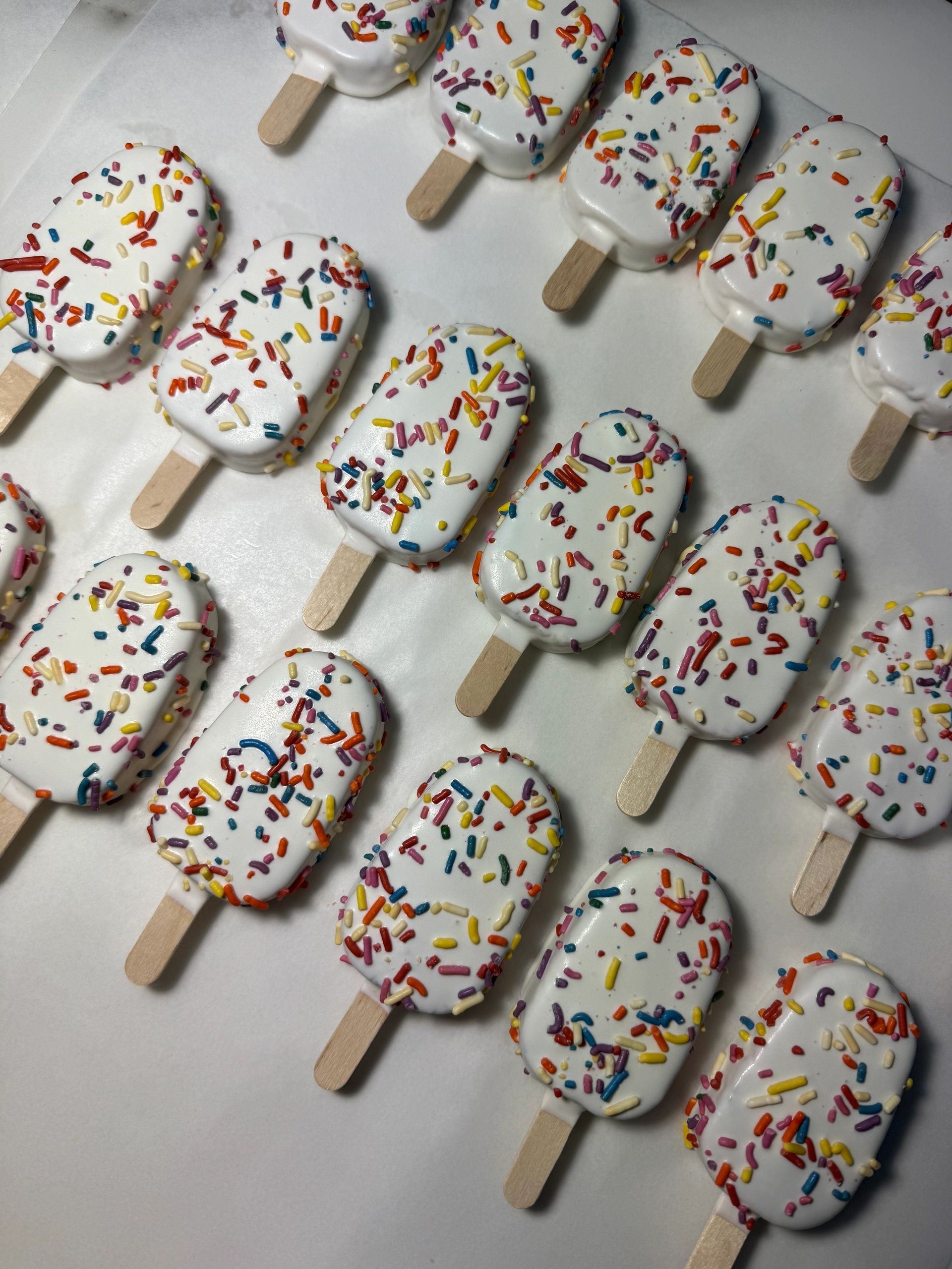 Miniature ice cream pops with white coating and colorful sprinkles.