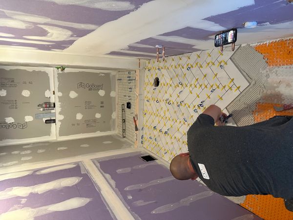 Man installing floor tiles in a small bathroom under construction.