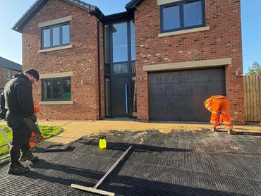 Employees putting down the resin on a new resin bound driveway whilst slowly applying.