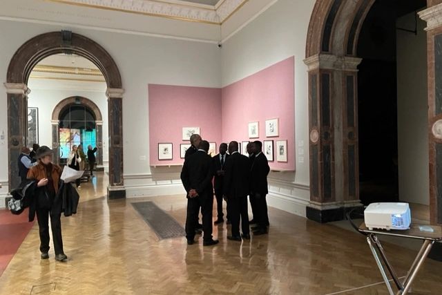 People gathered in an art gallery with paintings and arches.