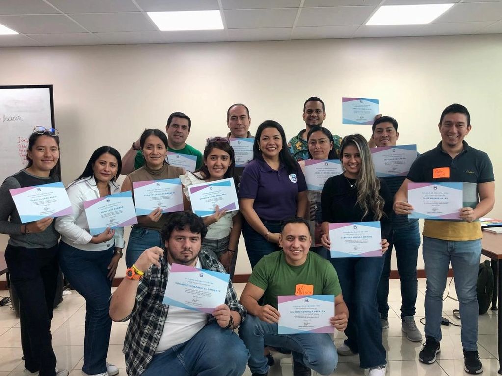 Group photo of smiling people holding certificates in a classroom setting.