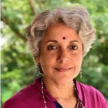 Portrait of a woman with gray hair and a bindi, wearing a magenta top.
