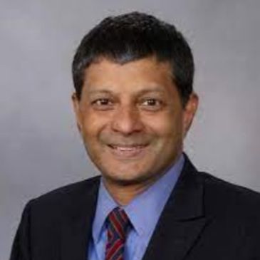 Professional man in suit and tie smiling against a neutral background.