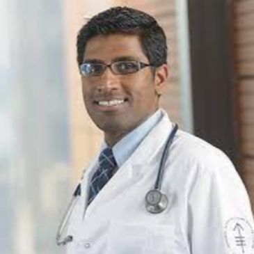 Smiling male doctor in white coat with stethoscope and glasses.
