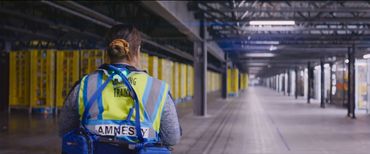 A person wearing a blue vest labeled 'Amnesty' in a large, empty industrial space.