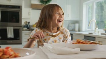 A happy young girl enjoying a meal at the kitchen table.