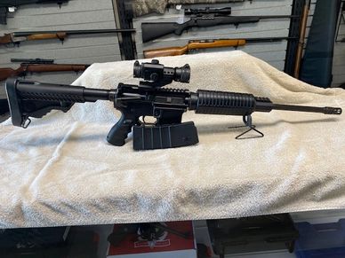 Black tactical rifle with scope resting on a white cloth.