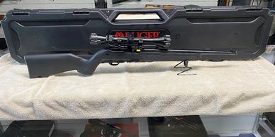 A black scoped rifle displayed in front of a police-branded case.