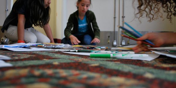 Children sitting on the floor surrounded by art supplies, focused on drawing.
