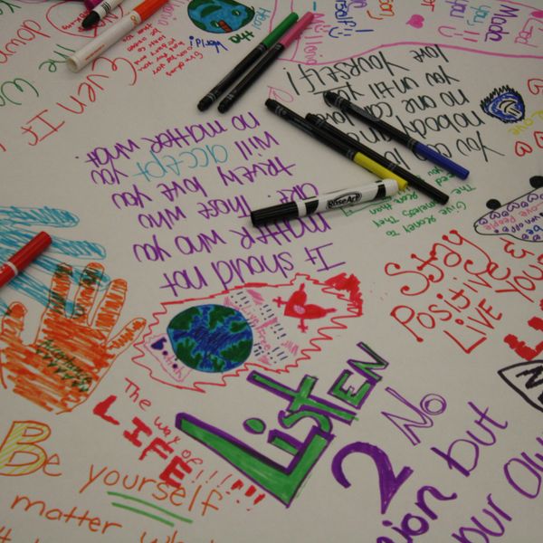 Colorful positive messages and drawings on a large white sheet with markers scattered around.