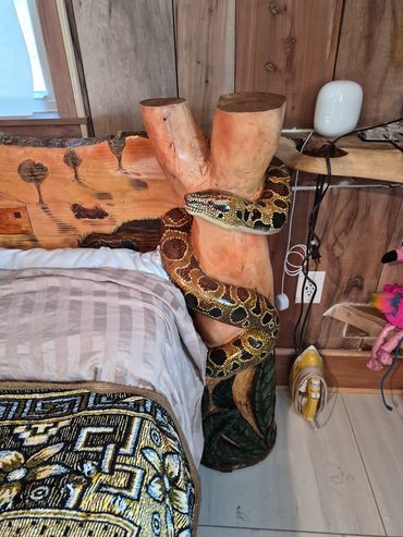 A carved wooden snake sculpture wrapped around a tree trunk beside a bed.
