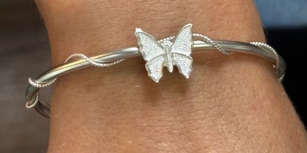 Silver bracelet with a butterfly charm on a wrist.