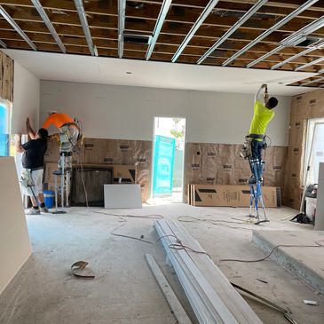 Three workers installing drywall in a room under construction.