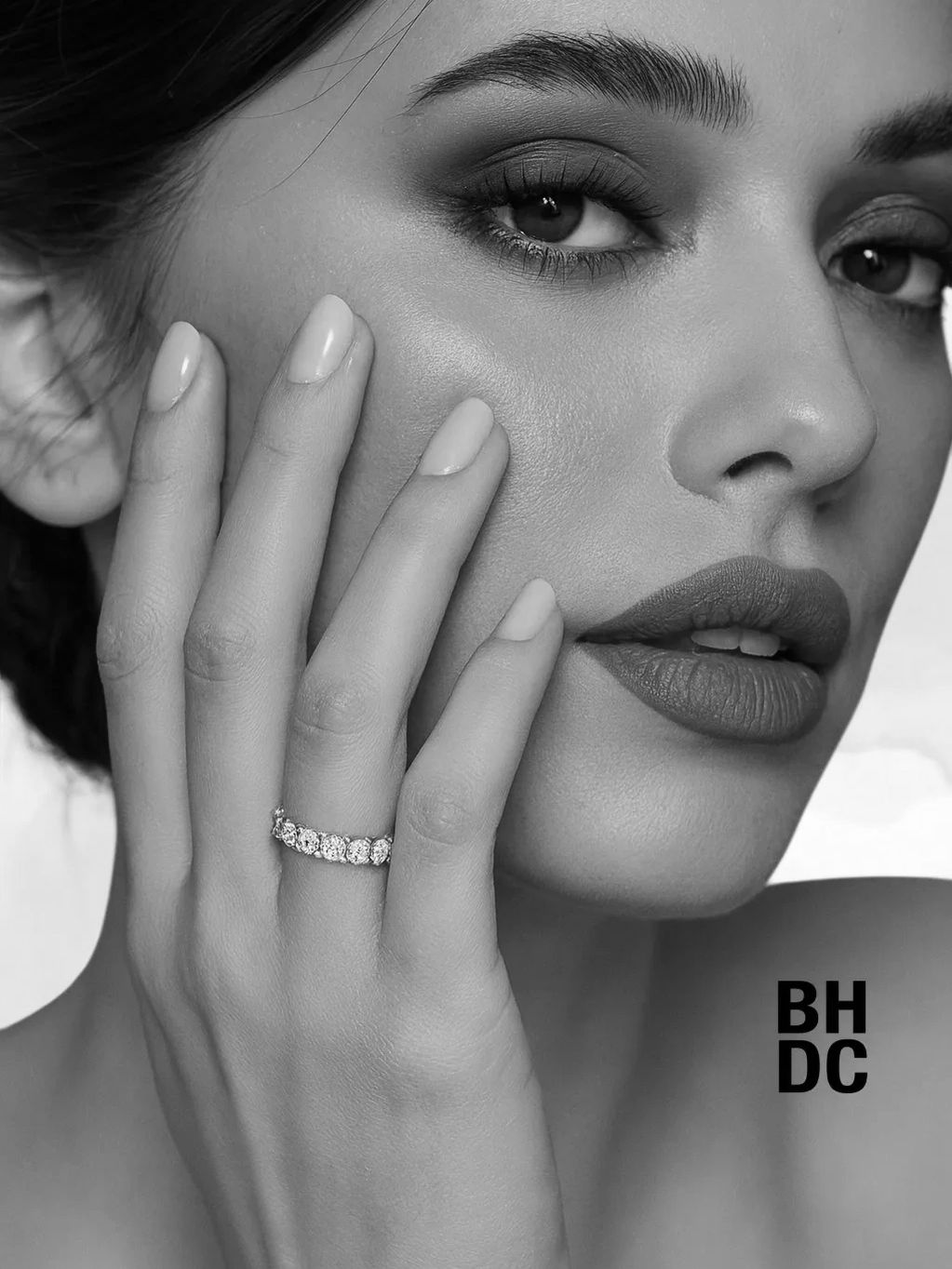 Close-up of a woman with elegant makeup and a diamond ring on her finger.