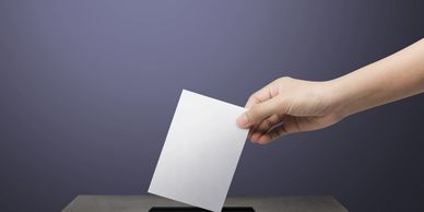 A hand placing a white ballot into a voting box.