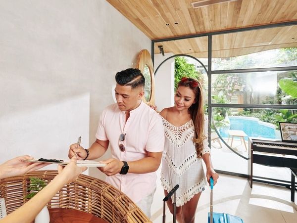 A man signs a document at the hotel reception while a woman stands beside him, smiling.