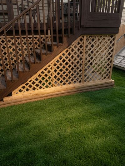 Wooden deck stairs with lattice panel and green grass.