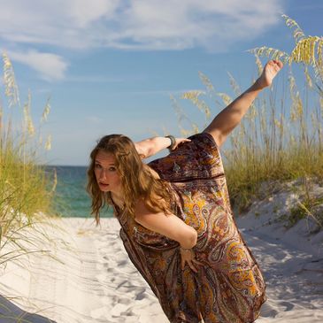 Woman balancing on one leg on a sandy beach path.