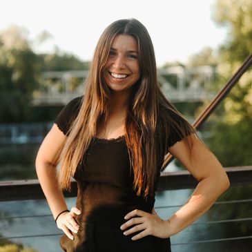 Smiling woman with long hair in black top outdoors.