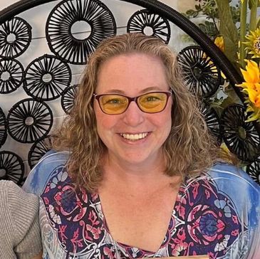 Smiling woman wearing glasses with yellow lenses and floral blouse.