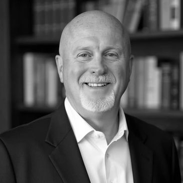 Smiling bald man in suit with bookshelf background.