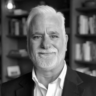 Portrait of a smiling elderly man with white hair and beard in a suit.