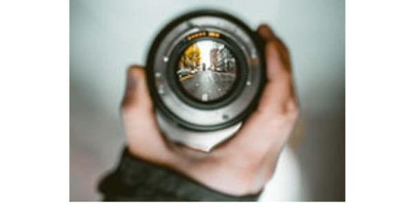 Person's hand holding  a camera lens focused on subject.