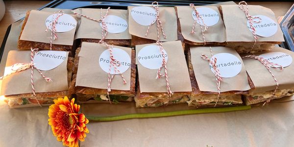 Wrapped Prosciutto and Mortadella sandwiches with a decorative flower.