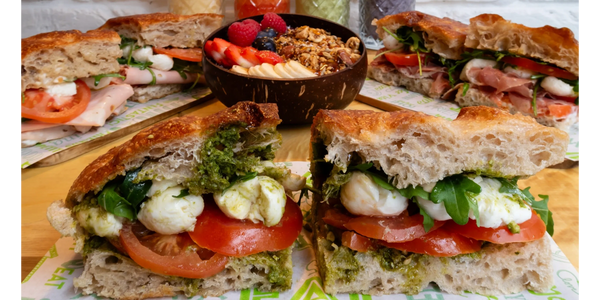 Variety of fresh sandwiches, smoothies, and a fruit bowl arranged on a wooden table.