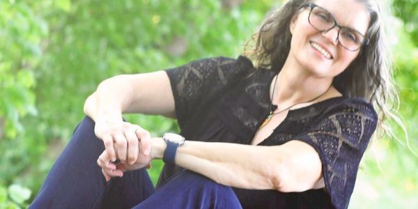 Smiling woman with glasses sitting outdoors on grass.
