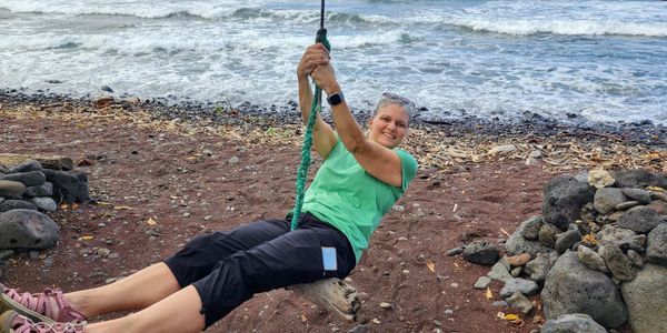 A woman enjoys swinging on a rope swing by the beach.