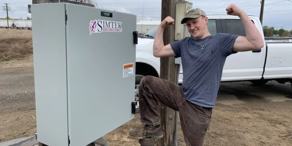 Man flexing muscles next to Simtek equipment outdoors.