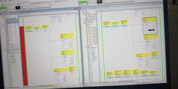 Dual computer screens showing programming diagrams with yellow highlights.