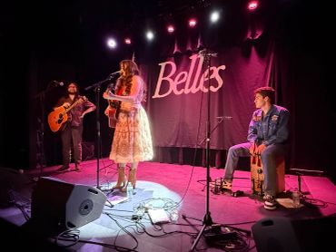 Musicians perform on stage under the sign 'The Belles'.