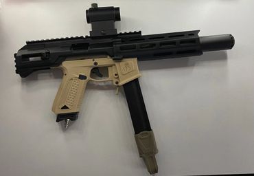 Compact black and tan airsoft gun with red dot sight and long magazine.