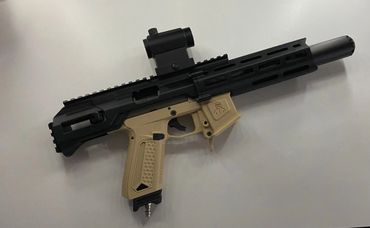 Compact black and tan airsoft or paintball gun with a red dot sight.