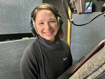 A smiling woman wearing headphones in a recording booth.