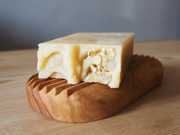 a close up image of handmade all natural herd and elder soap resting on a wood soap dish, on a pine e