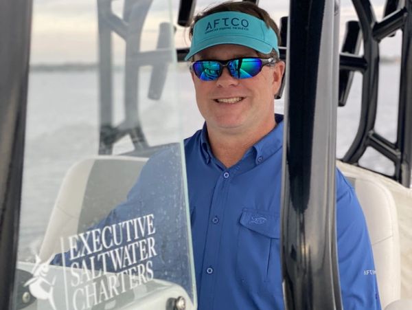 Man in blue shirt and visor on a boat smiling.