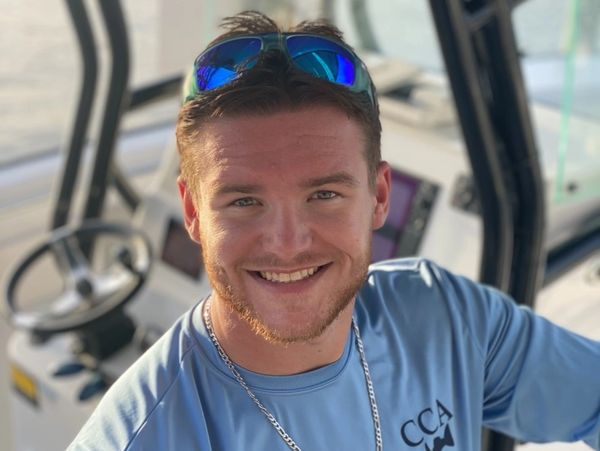 Smiling young man wearing sunglasses and a blue shirt on a boat.
