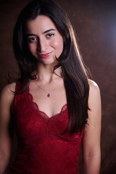 Young woman in a red lace dress smiling gently at the camera.