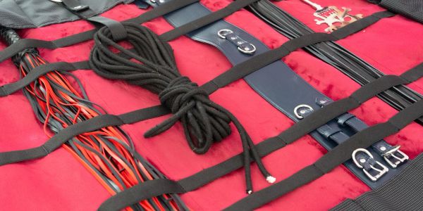 Floggers, ropes, and belts on a red surface.