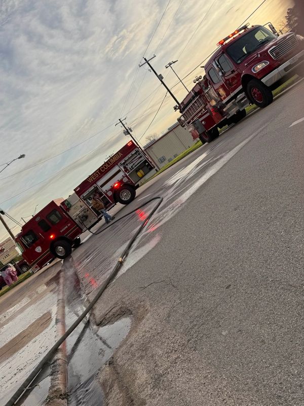 Fire trucks and a hose on a wet street at sunset.