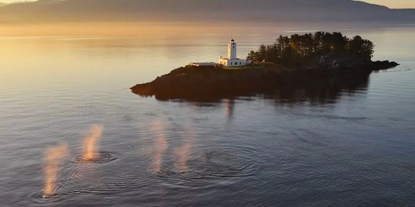 Lighthouse on a small island at sunset with mysterious steam rising from the water.