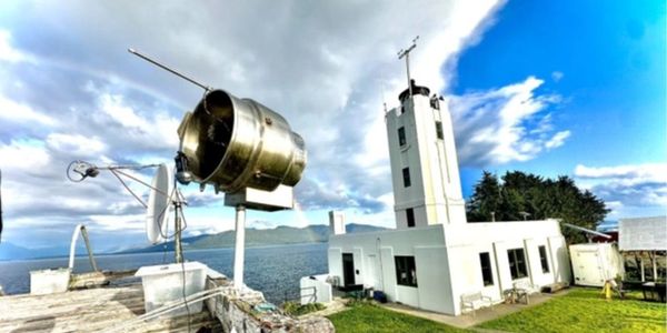 Lighthouse by the sea under a cloudy sky with a large light fixture.