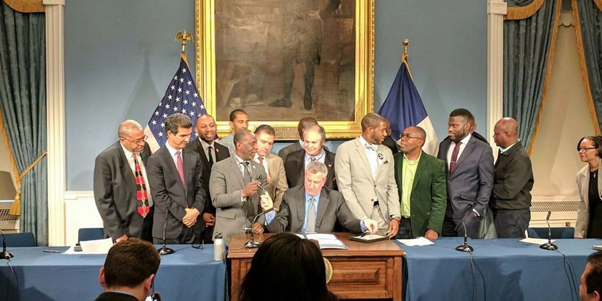 Mayor signs Commuter Van Reform on a desk, before several people. Nick is third from Mayor's left.