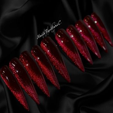 Glossy red stiletto nails with a glittery finish on a black satin background.