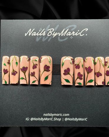 Set of nude-colored press-on nails with purple flower designs and green leaves.