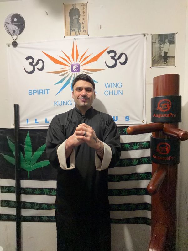 Man in martial arts attire posing in front of Kung Fu and Wing Chun banners.