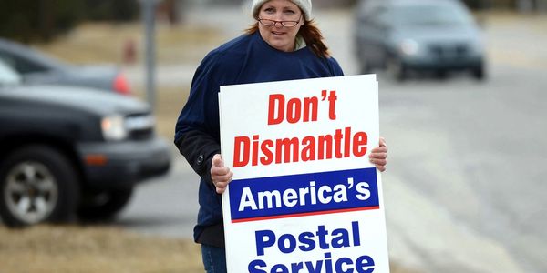 A woman carrying a sign that says, "Don't Dismantle America's Postal Service".